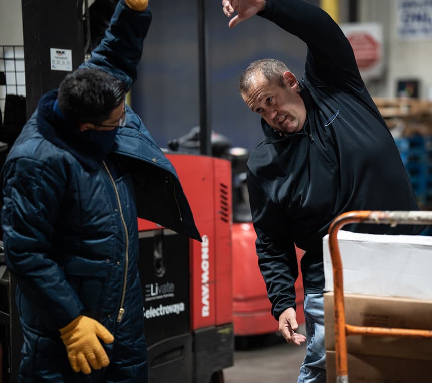 Two men stretching to prevent injury in a warehouse
