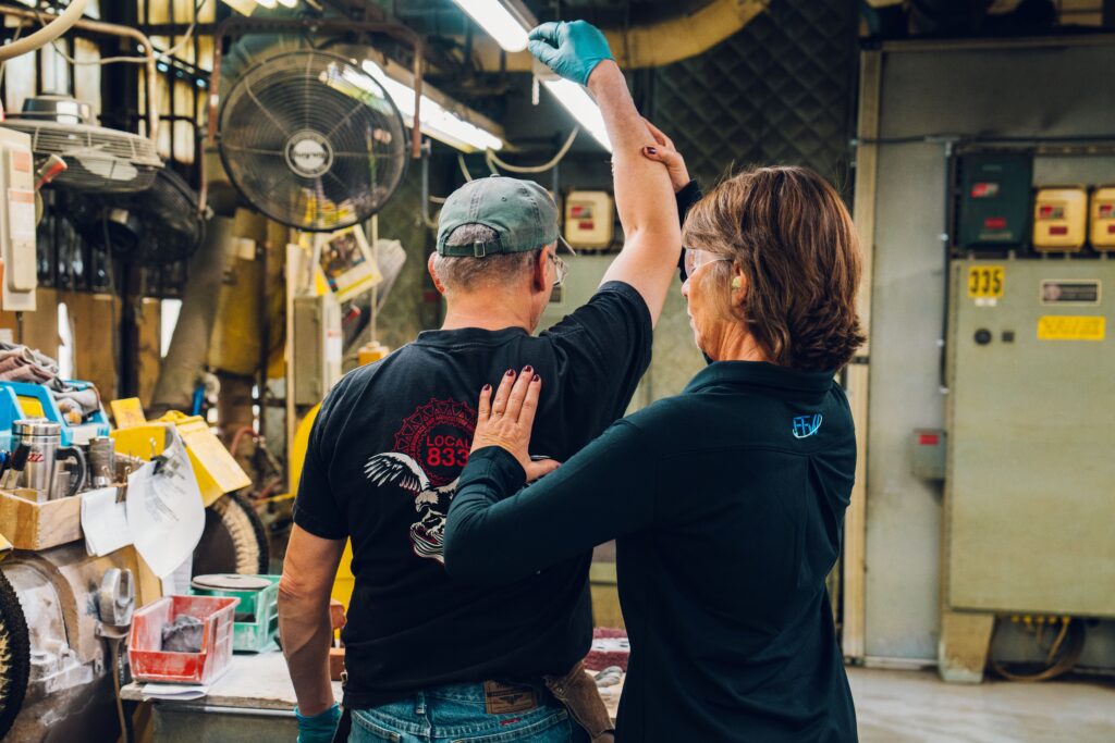 An occupational therapist assists a worker with a shoulder stretching exercise