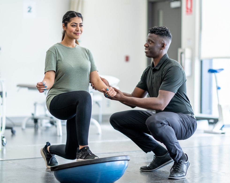 Woman lunging on a stability platform while her therapist helps her maintain her balance.