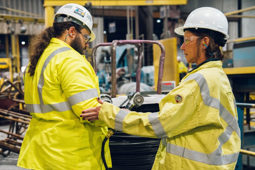 Two workers in safety gear standing next to each other in warehouse.