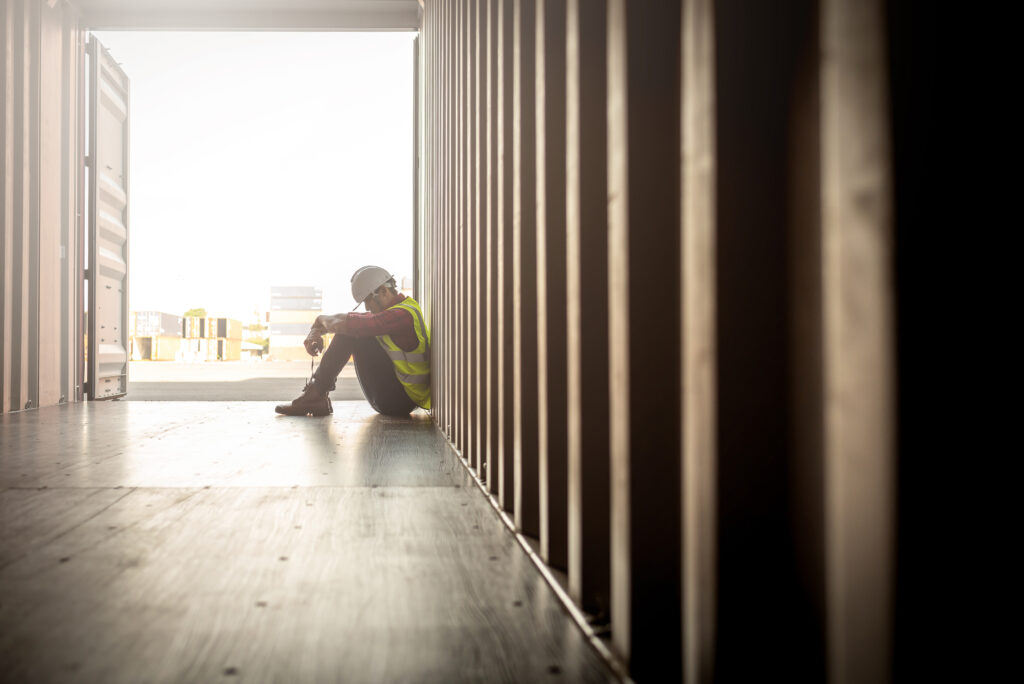 Stressed worker sitting in container box looking down.