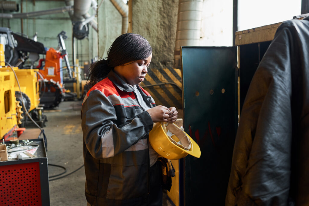Woman in uniform standing near her closet and taking off the work helmet after her work in factory