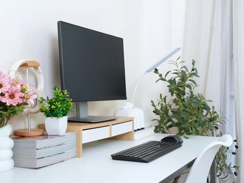Minimalist home office setup with monitor, keyboard, headphones, books, and potted plants. Bright, clean, and cozy workspace ideal for productivity and creative work.