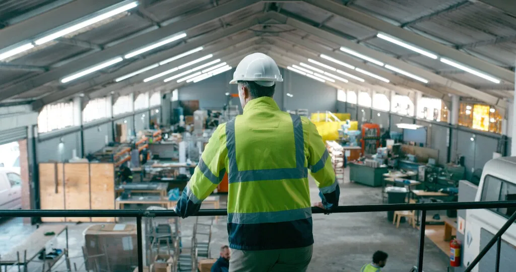 Back, technician and man in warehouse for manufacturing solution, planning and safety compliance. Engineer, person or supervision on factory balcony for supply chain, quality assurance or inspection.