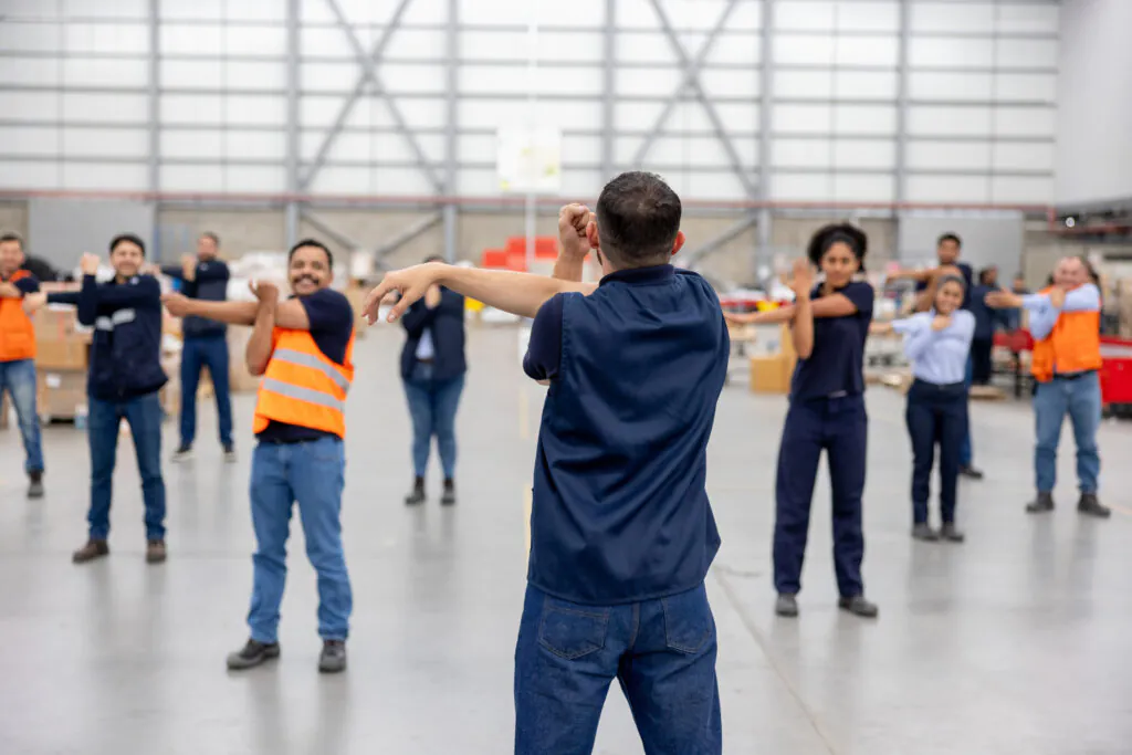 Group of warehouse workers stretching during an active pause following an instructor