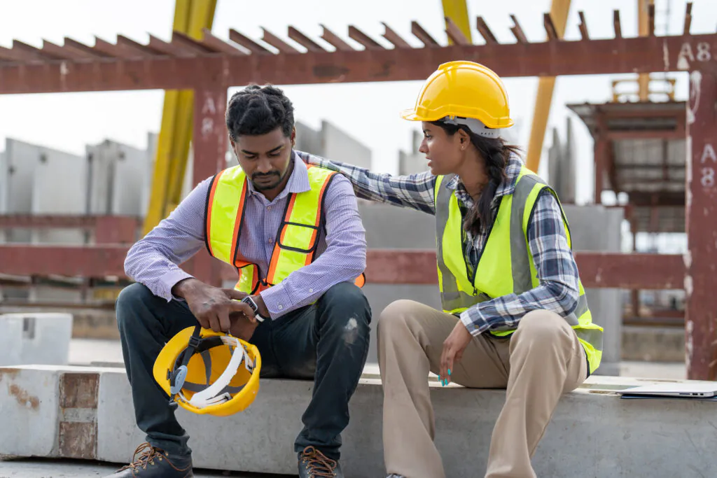 Asian Indian man worker feeling sad and upset while sitting at construction site. Female worker colleague supporting and consolation him.